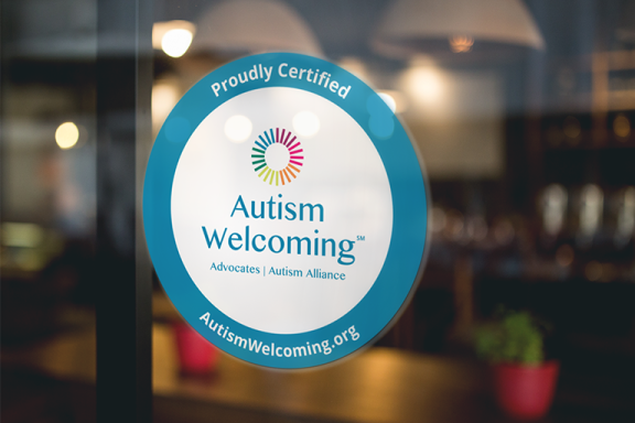 A photo of a decal with the Autism Welcoming logo on a glass window