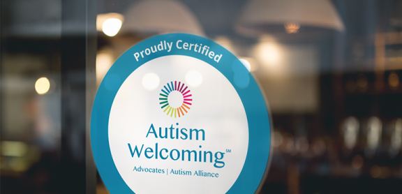 A photo of a decal with the Autism Welcoming logo on a glass window